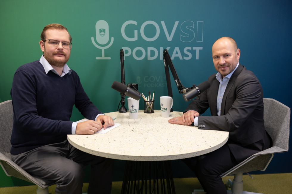 Dva moška sedita za okroglo mizo na kater sta dva mikrofona, v ozadju napis GOVSI podkast.