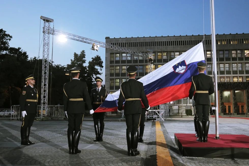 Šest vojakov častne straže sodeluje pri dvigu slovenske zastave na drog na Trgu republike pred stavbo parlamenta.
