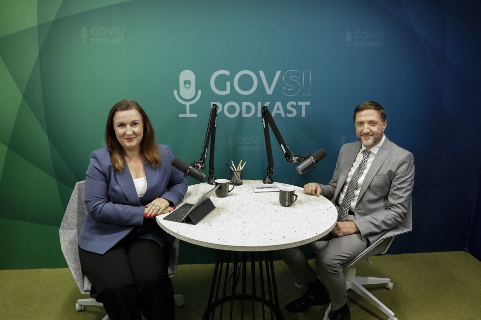 Ženska in moški sedita za okroglo mizo z mikrofonoma.