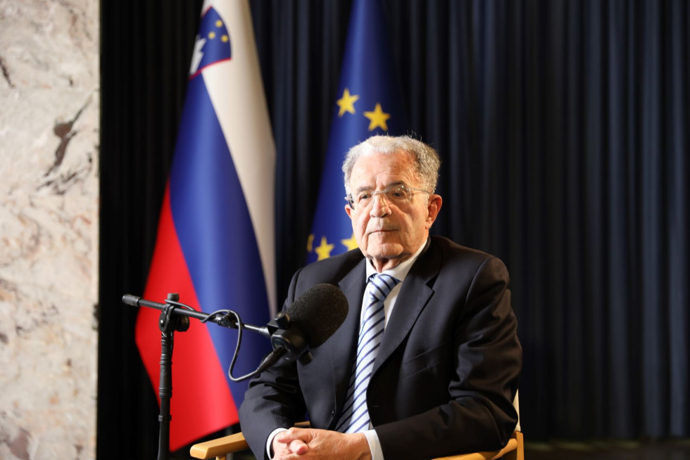 Romano Prodi sedi, pred njim je mikrofon