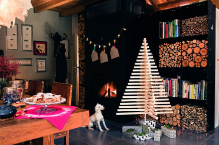  A living room with a festively decorated dining table. A wooden fir tree stands in the middle of the room, next to it sits a dog.