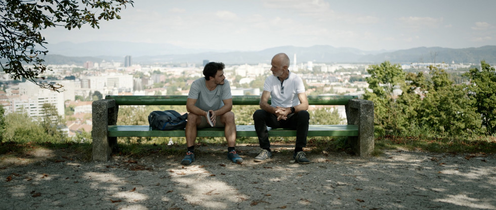 Glavni junak Andraž ob prvem srečanju z Andrejem Štremfljem na Ljubljanskem gradu. Sedita na klopci v parku ob gradu.
