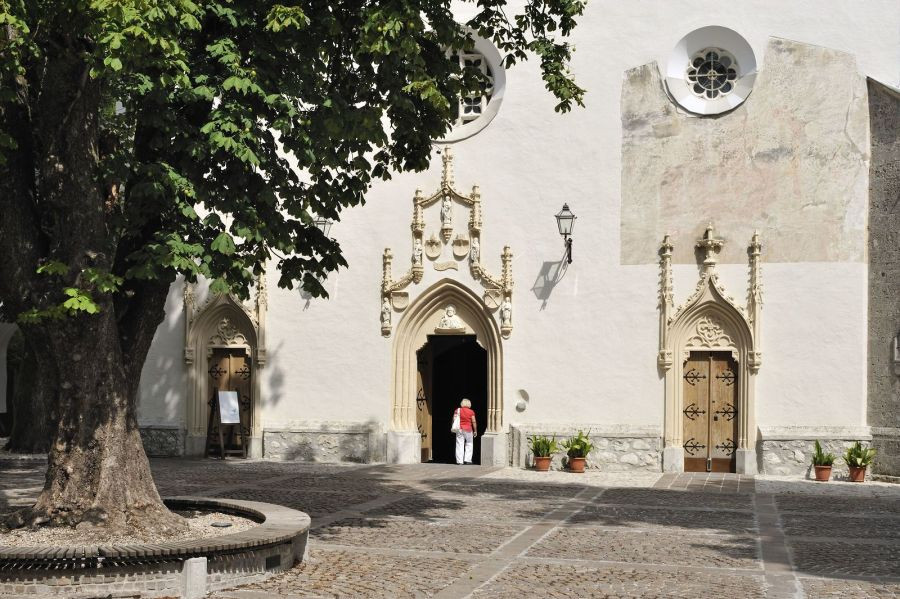 The façade of the church with the entrance, near the church stands a tree.
