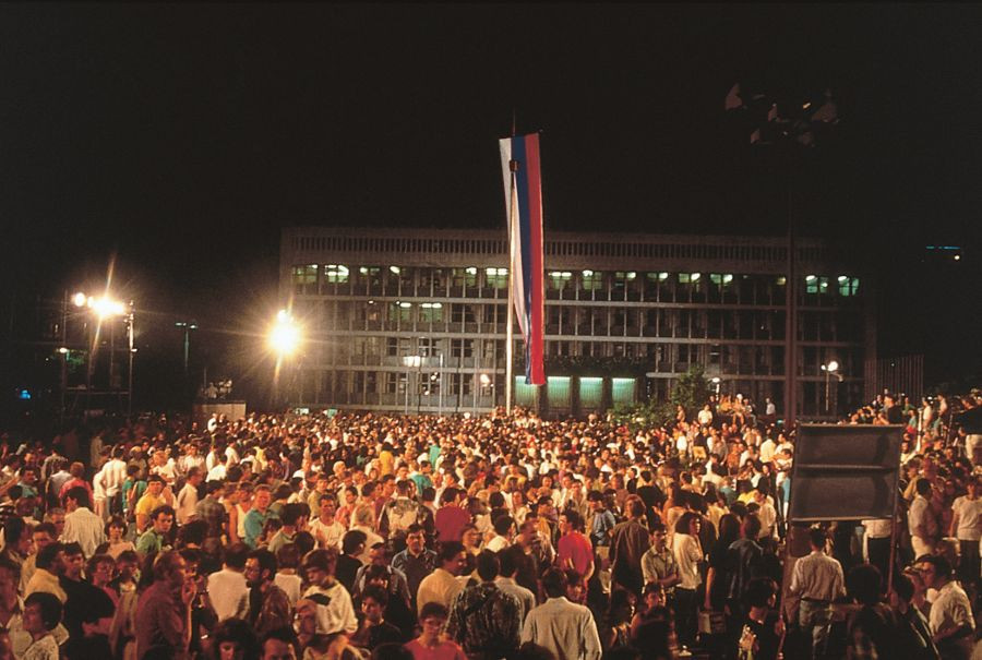 A crowd in Republic Square. There's a parliament in the background and a raised flag.