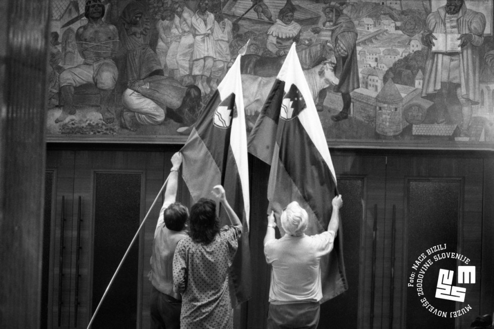 Moški in dve ženski izobešajo v državnem zboru dve zastavi RS.