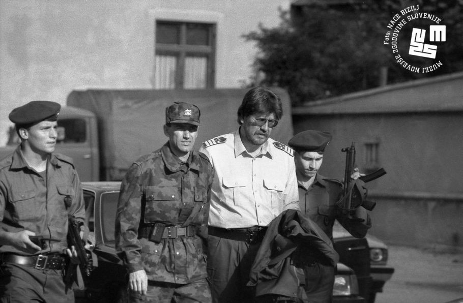 Dva vojaka, Janez Janša v vojaški uniformi in Igor Bavčar hodijo zunaj.