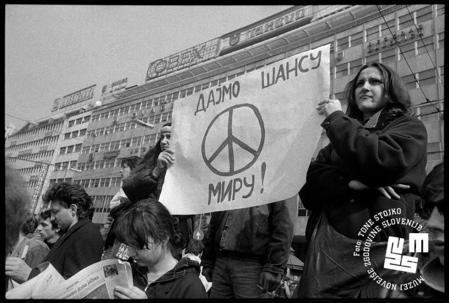 Protestniki, dva držita v rokah napis Dajmo šansu miru z znakom mir.