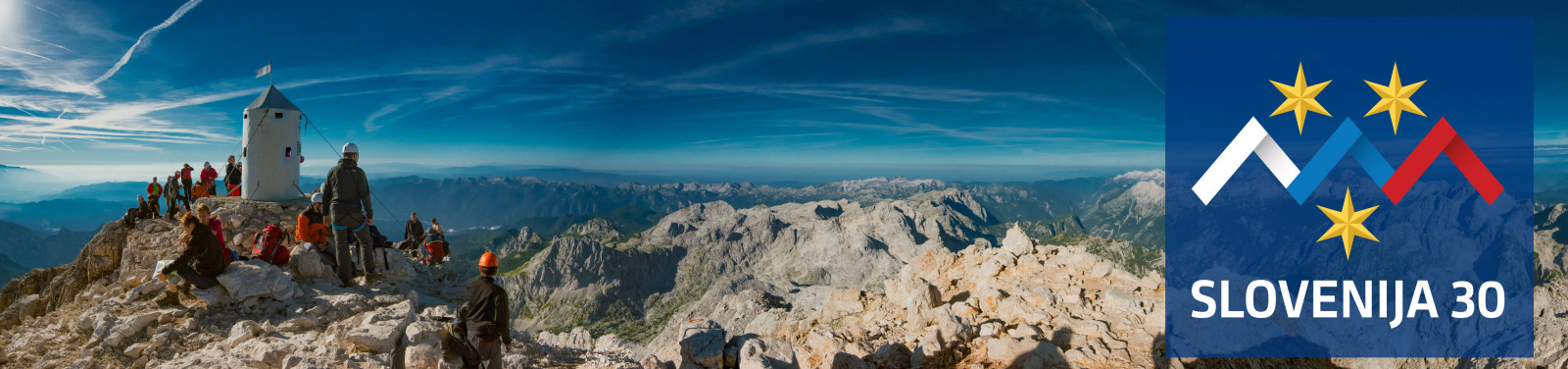 The summit of Triglav with the Aljaž Tower, people sit and stand. Mountain view.