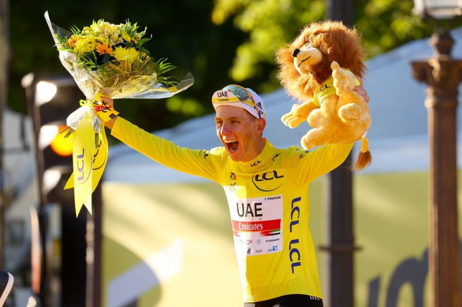 Tadej Pogačar on the winning stage with a bouquet and mascot in his hands.