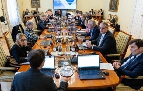 seja vlade cover (Government officials seated around a long wooden conference table during a formal cabinet meeting, each working on laptops, with documents and water pitchers on the table.)