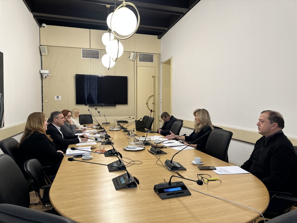 Udeleženci sestanka sedijo za ovalno mizo