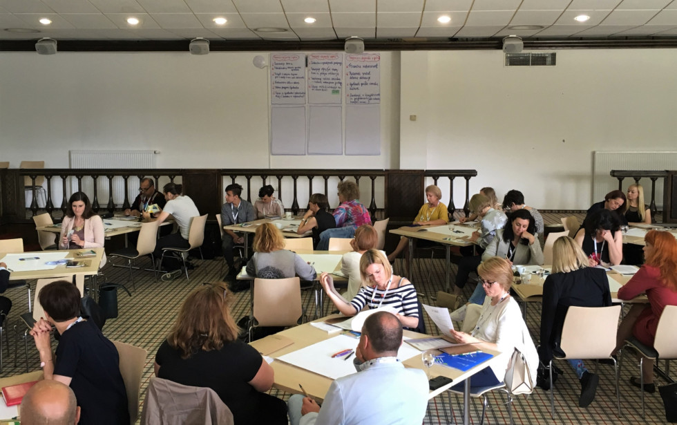 Udeleženci sedijo za mizami po skupinah