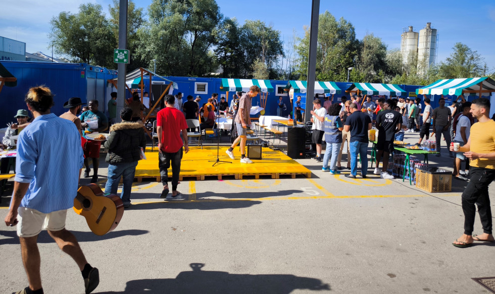 Nastanjeni in obiskovalci pred azilnim domom, v ozadju stojnice nevladnih organizacij