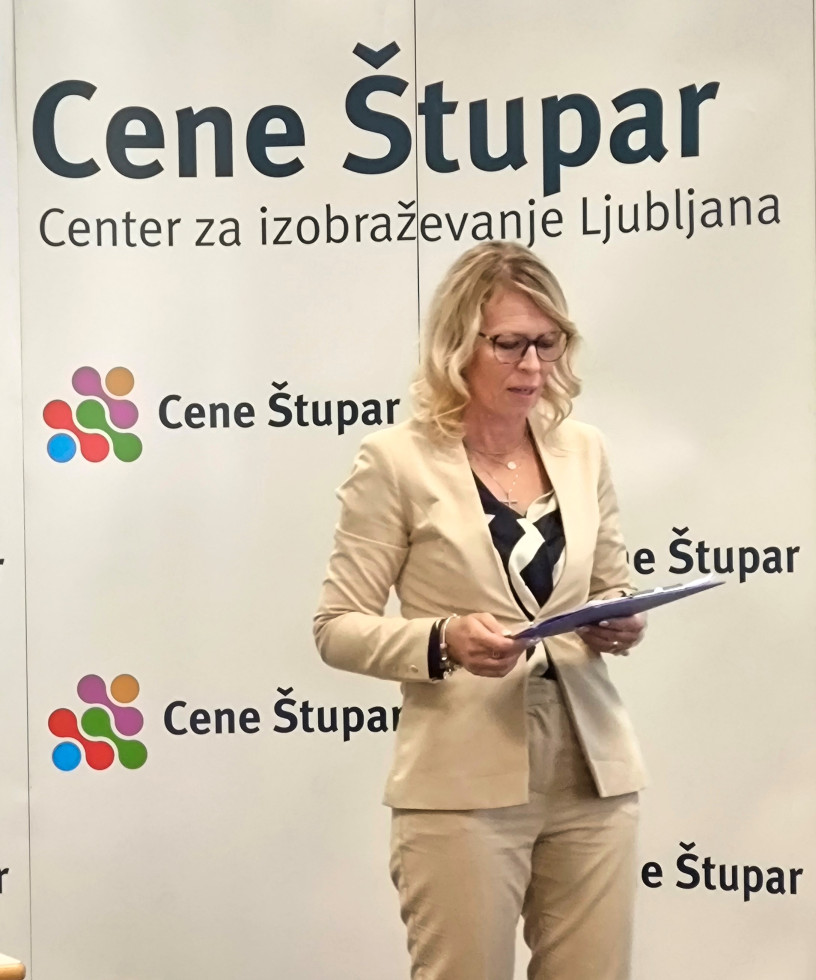 Ženska na odru nagovarja skupino ljudi