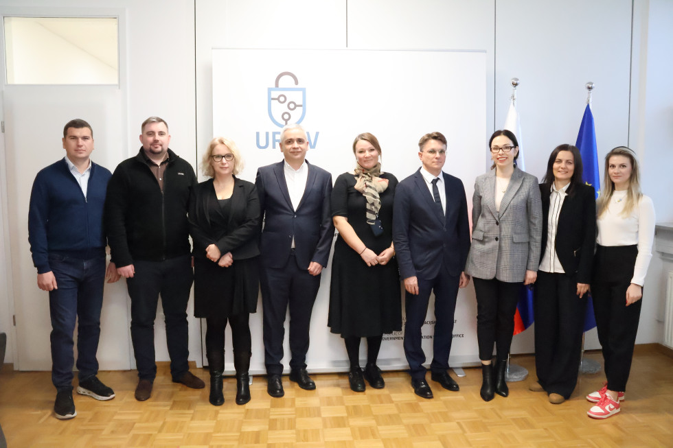 Skupinska slika. Udeleženci bilateralnega srečanja stojijo pred panojem in zastavama na URSIV.