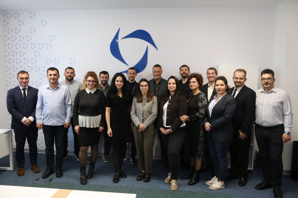 Moški in ženske skupaj stojijo eden zraven drugega. Belo ozadje z modrim logom.