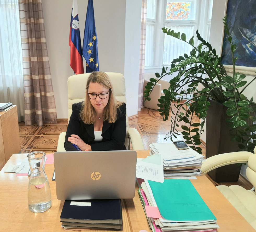 Ministrica pred računalnikom, za njo slovenska in evropska zastava.