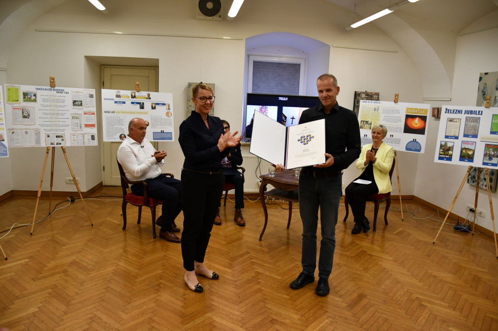 G. Rihar drži priznanje, ministrica na levi strani ploska, v ozadju sedijo razpravljalci na okrogli mizi.