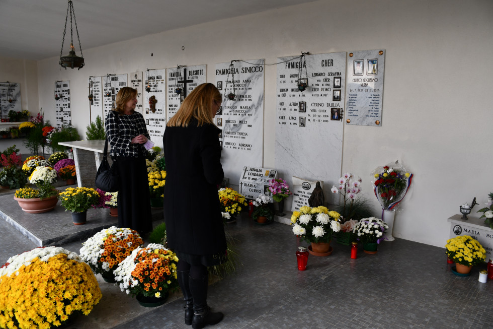 Ministrica s sklonjeno glavo pred nagrobnim spomenikom Vilejam Černa. Spodaj svečke in rože.
