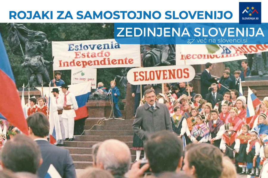 Nastopajoči v narodnih nošah, slovenske zastave, napisi v španščini, v ozadju na levi spomenik 