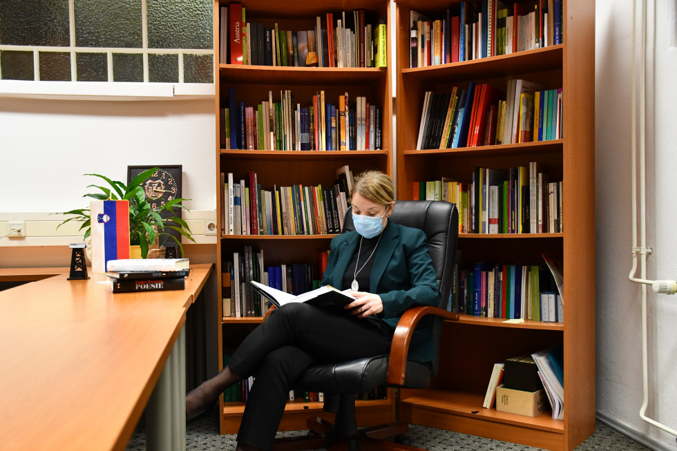 ministrica sedi s knjigo v roki v knjižnjici.