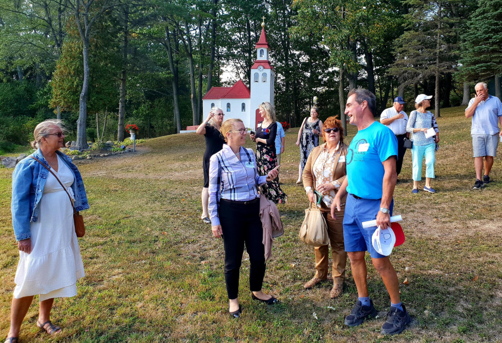 Ministrica, generalna konzulka in rojaki med pogovorom v parku, v ozadju cerkvica.