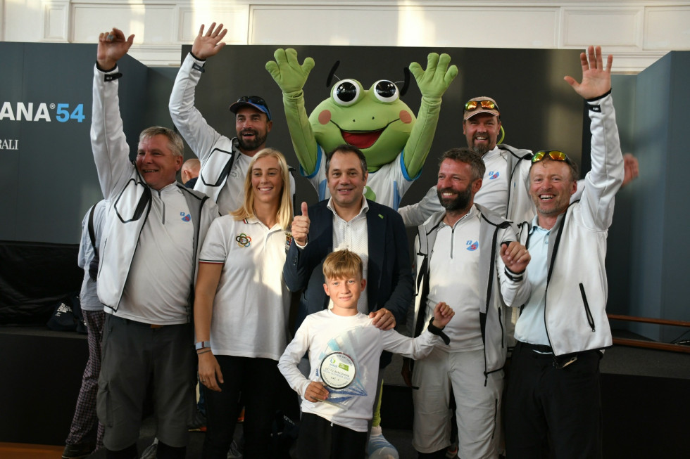 Minister Arčon z udeleženci regate. Stojijo in držijo roke v zrak, za ministrom maskota žaba.