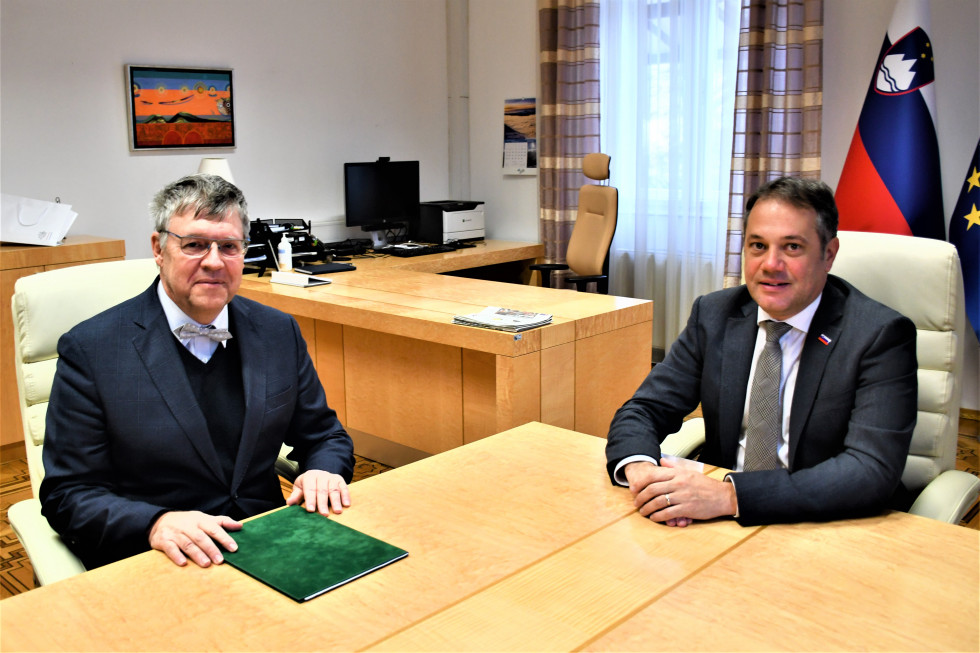 Juraj Chmiel in Matej Arčon sedita za mizo, v ozadju slovenska in evropska zastava.