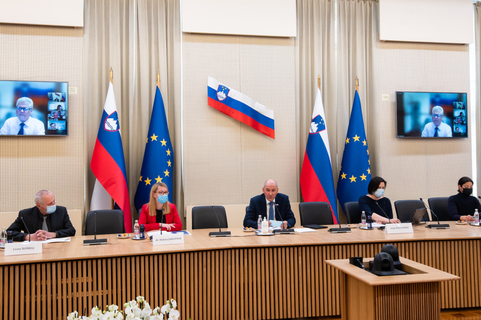 Ministrica in predsednik sedita za mizo, za njima slovenske in evropske zastave na vsaki strani in slovenska na steni.