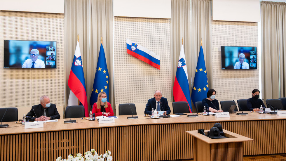 Ministrica in predsednik sedita za mizo, za njima slovenske in evropske zastave na vsaki strani in slovenska na steni.