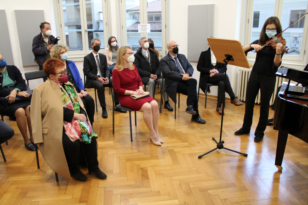 Udeleženci, na desni dekle, ki igra violino. Ministrica na sredini, sedi, v rdeči obleki.