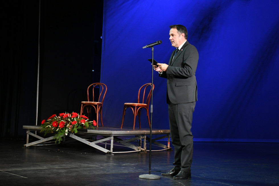 Minister Matej Arčon med govorom na odru, pred njim mikrofon.