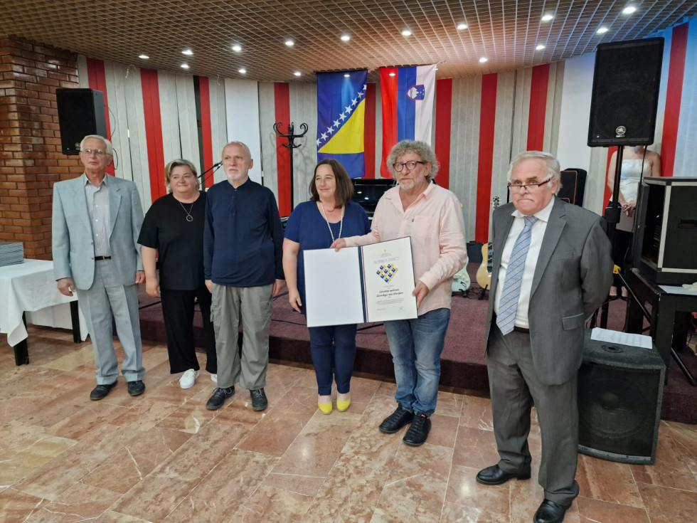 Državna sekretarka s predstavniki društva. V rokah držijo priznanje.