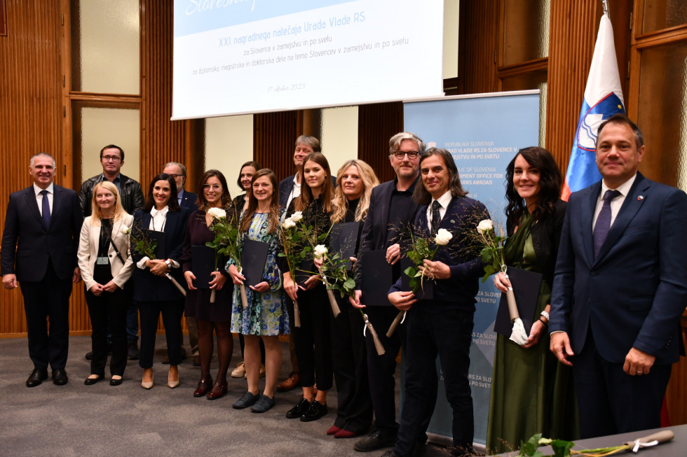 Minister in predsednik državnega sveta z nagrajenci in člani strokovne komisije. Nagrajenci v rokah držijo priznanja in rože, za njimi letak urada in slovenska in evropska zastava.
