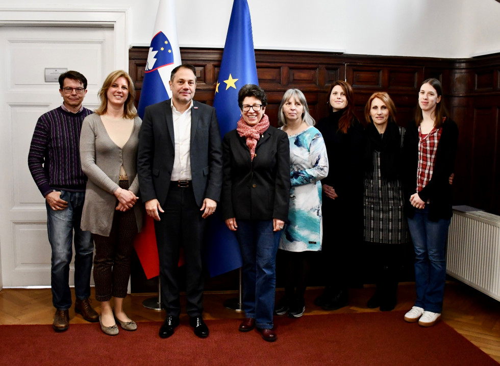 Udeleženci sestanka stojijo pred slovensko in evropsko zastavo v avli urada.