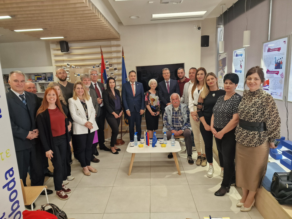 Udeleženci srečanja stojijo pred zastavami v prostoru, kjer je potekal pogovor.