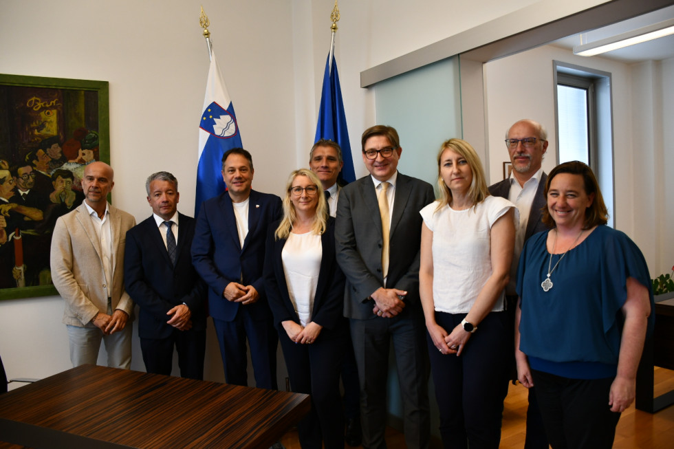 Minister, državna sekretarka, generalni konzul in župani stojijo pred slovensko in evropsko zastavo.