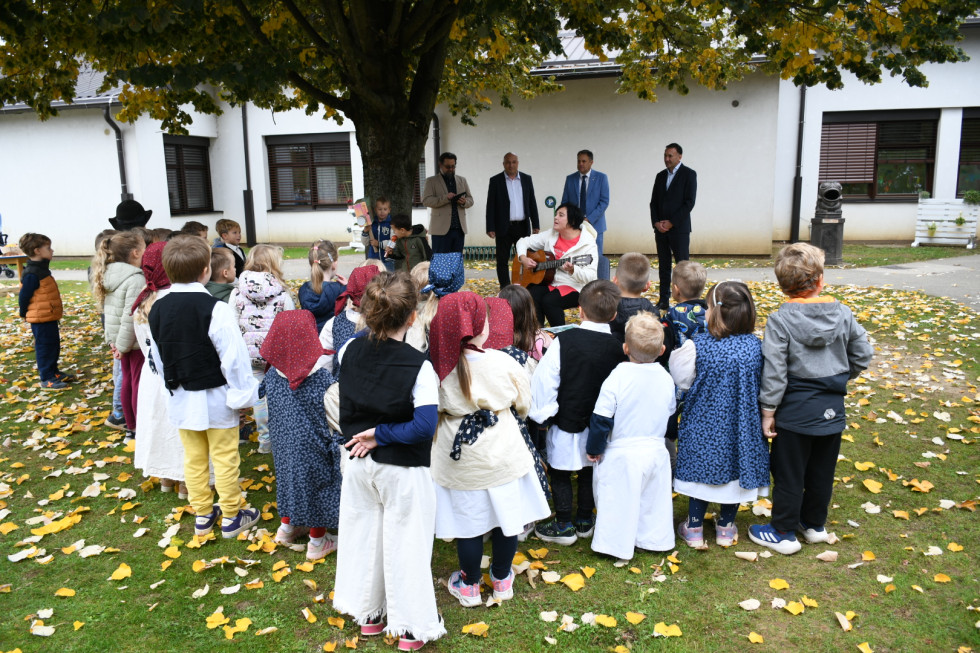 Otroci oblečeni v noše med tem ko pojejo ministru, minister, ravnatelj gledata.