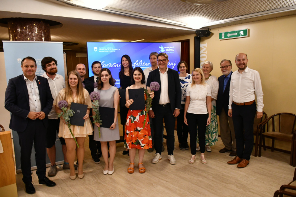 Skupinska fotografija nagrajencev, ki držijo diplome in šopke, z ministrom Arčonom in člani strokovne komisije na podelitvi nagrad.