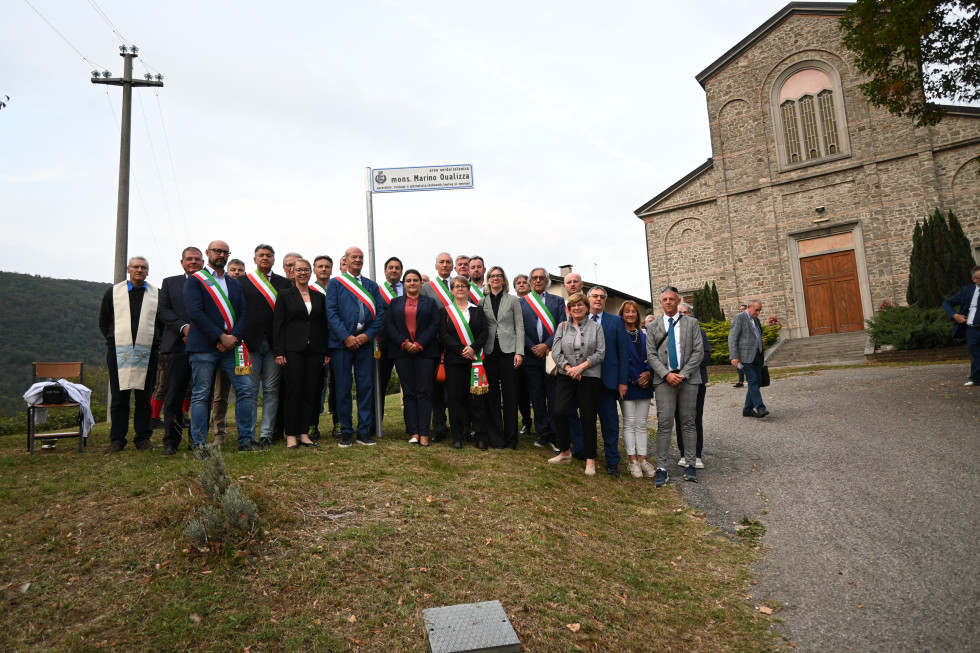 Ministrica, državna sekretarka, župani in drugi pod znakom msgr. Marina Qualizze. Zadaj cerkev.
