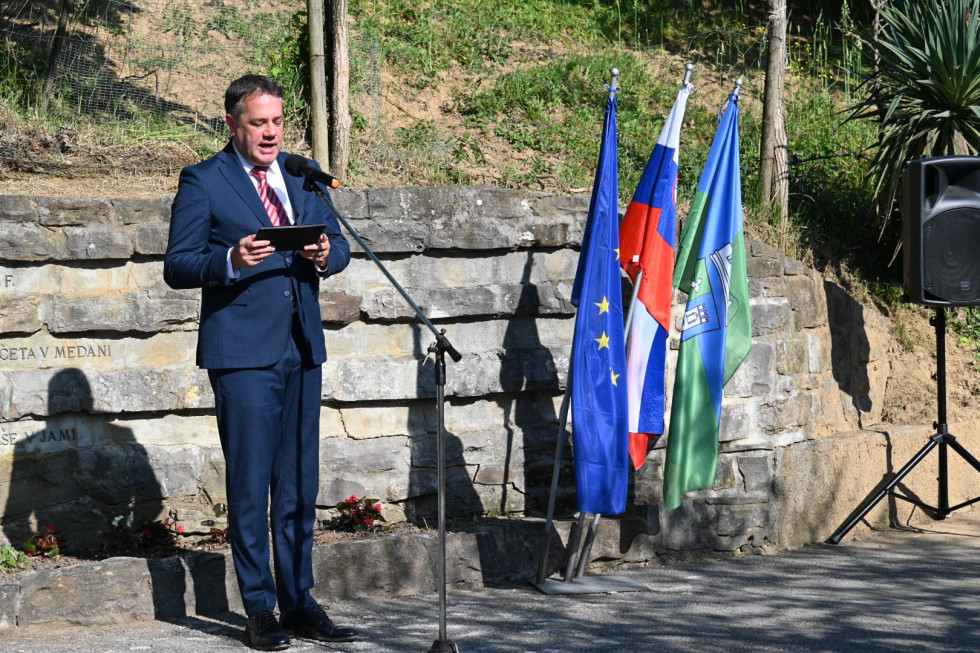 Matej Arčon med govorom pred obeležjem, na desni zastave.