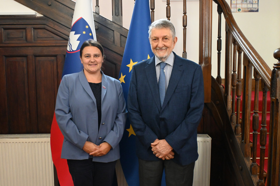 Ministrica in gospod Šalej pred zastavam slovensko in evropsko v avli urada.