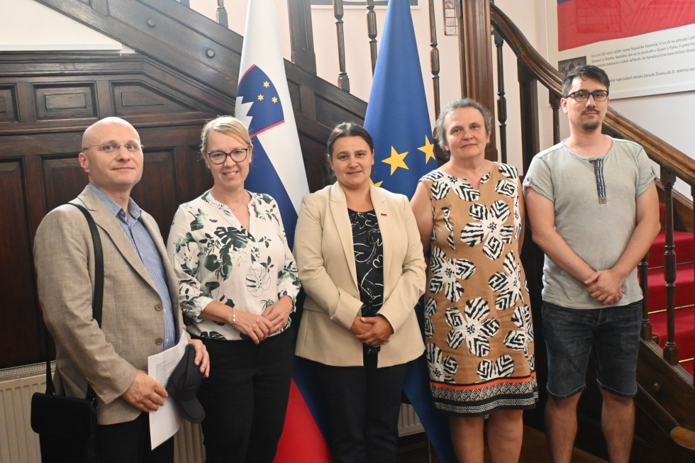 Gostje z ministrico in državno sekretarko pred zastavami v avli urada.