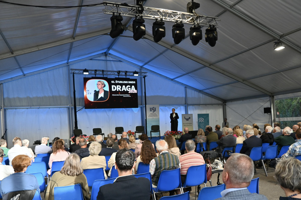 Za govornico državna sekretarka, na ekranu Draga, obiskovalci.
