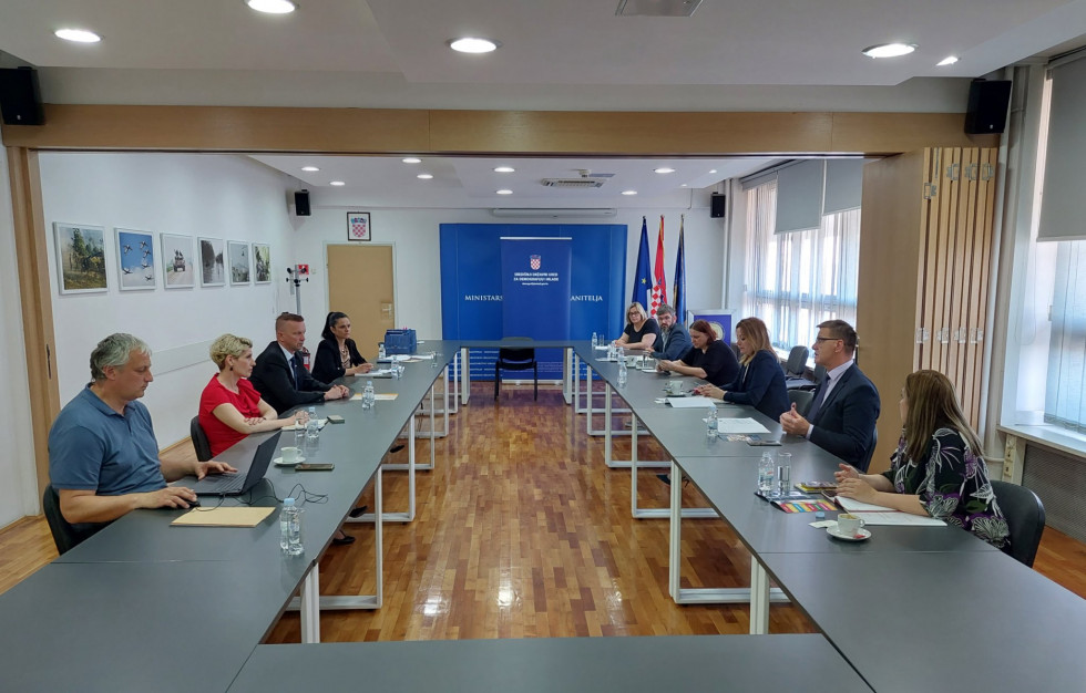 Predstavniki Urada za demografijo sedijo za mizo s hrvaškimi kolegi, barvna slika.