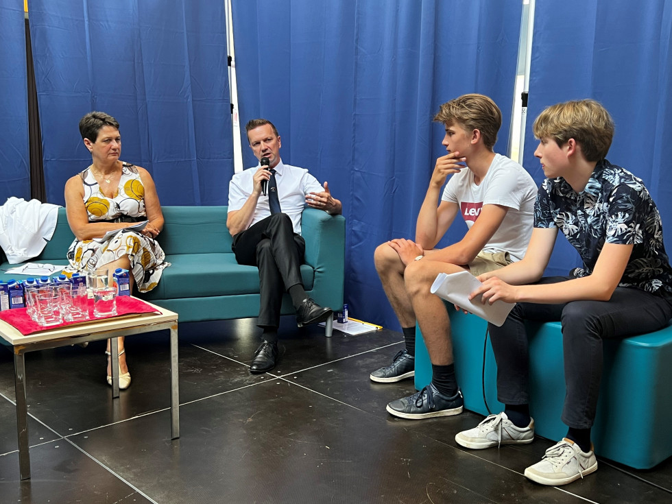 Danilo Lončarič sedi z mikrofonom v roki za mizo z mladimi in se z njimi pogovarja.